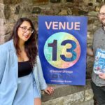 Vanesa Kelly and Ian Garrett stand outside Harry Younger Hall with a Venue 13 sign and the 2025 Fringe guide.